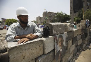 Members of the Muslim Brotherhood and supporters Mursi sit on a barrier they erected at an entrance near his poster at the Rabaa Adawiya square in Cairo